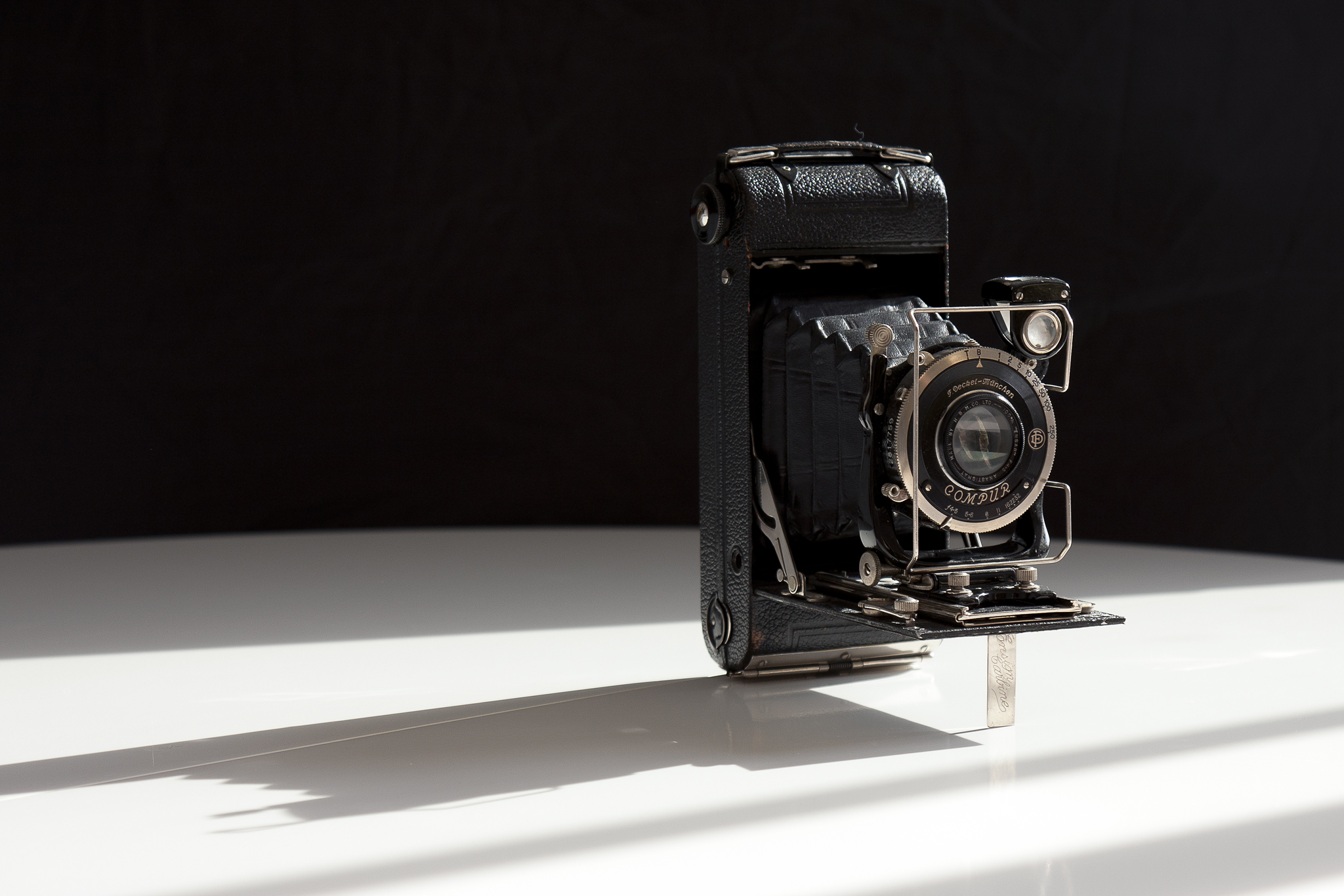 Un appareil photo vintage sur une surface blanche, avec un arrière-plan sombre, mettant en valeur son design classique.