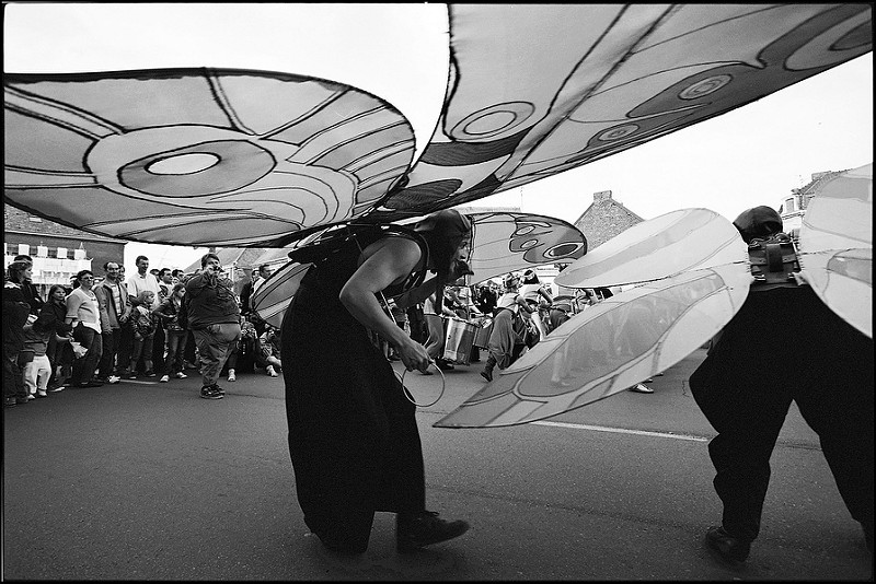 Une personne en costume avec de grandes ailes de papillon participent à une parade, entourée de spectateurs.