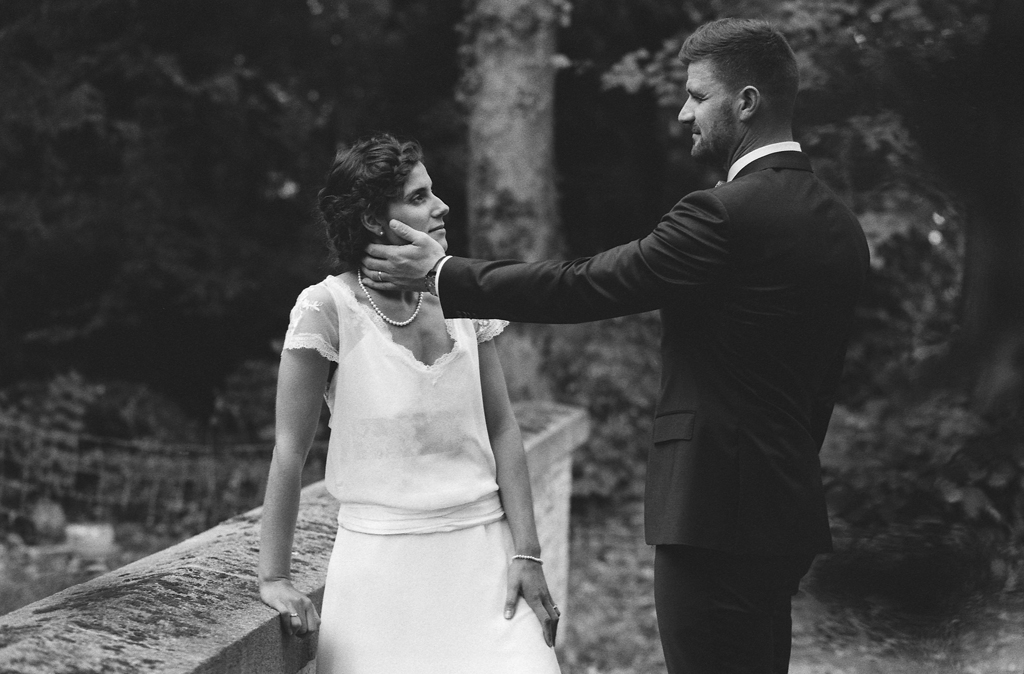 Un couple élégant en noir et blanc, échangeant un moment tendre dans un cadre naturel. Photographie argentique.