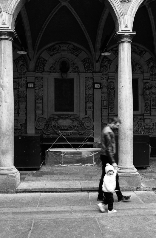 Un homme marche avec un enfant dans une ruelle à l'apparence historique, sous des arches décorées.