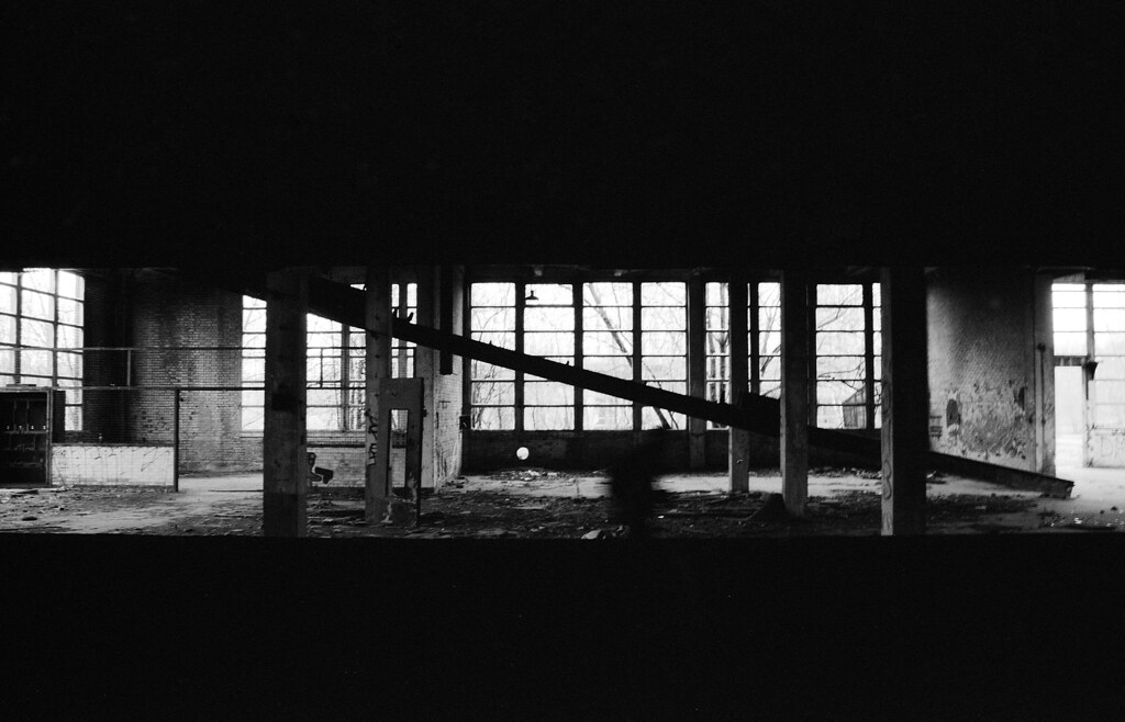 Photographie d'urbex en noir et blanc argentique. usine abandonnée et une silhouette floue cadre dans le cadre.