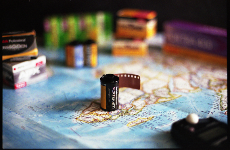A roll of Portra 400 film on a map, surrounded by various other film canisters and a light meter.