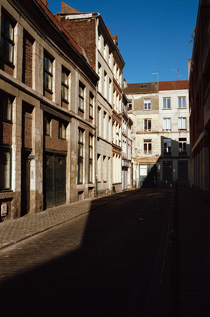 Vue d'une rue pavée bordée de bâtiments anciens sous un ciel bleu clair.