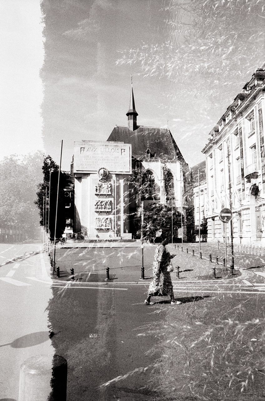 Double exposition en noir et blanc d'une rue à Lille, avec une femme marchant devant un bâtiment historique et des éléments d'arrière-plan texturés.