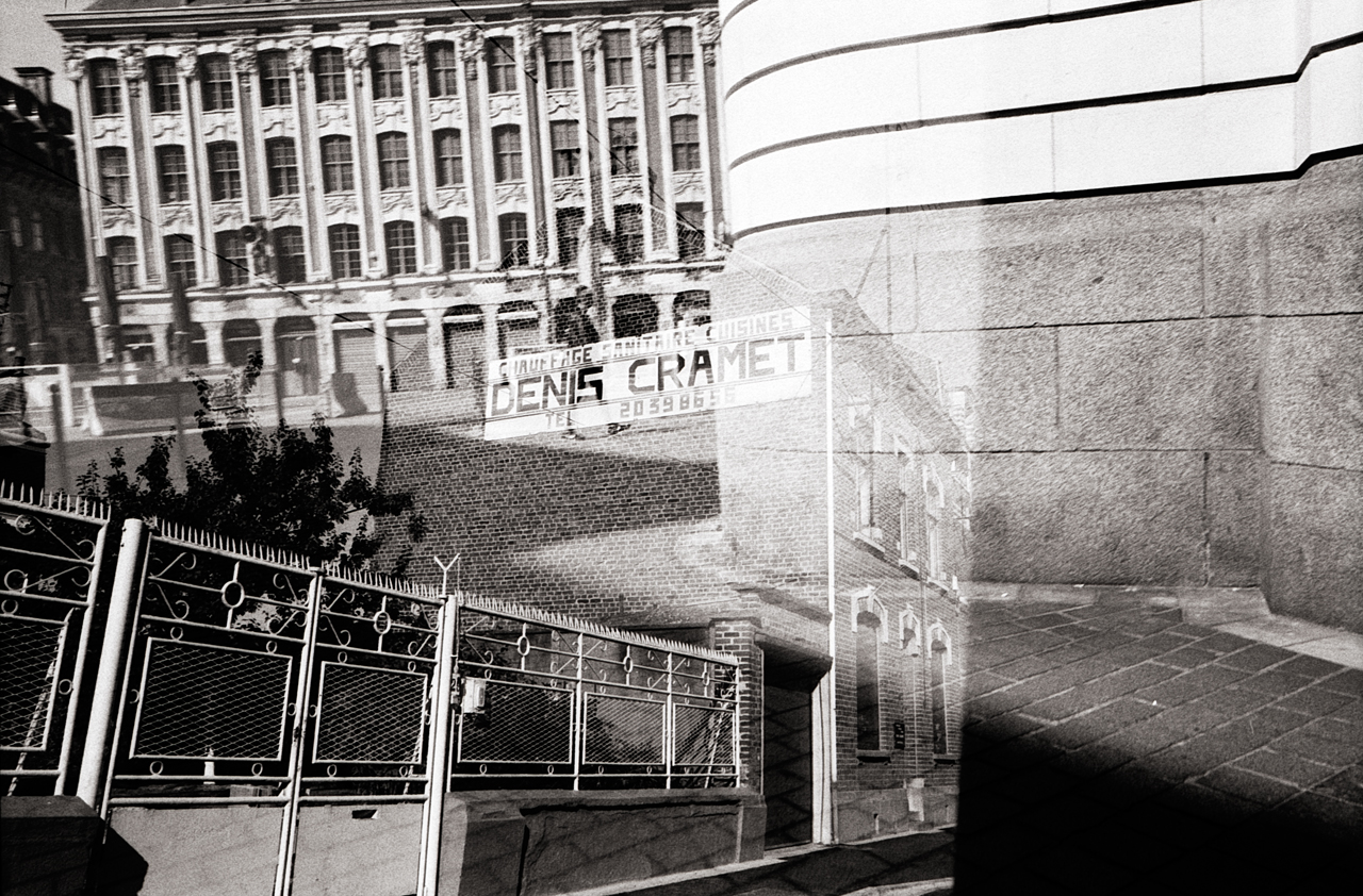 Double exposition en noir et blanc d'une scène urbaine, montrant un bâtiment ancien et une affiche floue, avec des éléments de la rue superposés.
