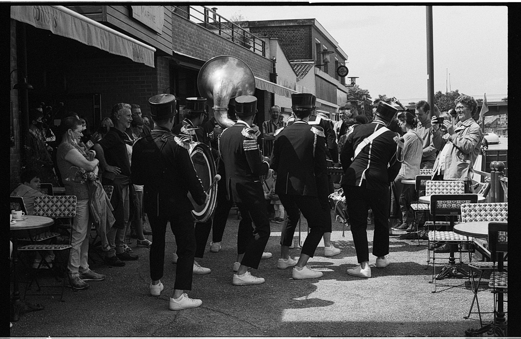 Un groupe de musiciens en tenue formelle, jouant de la musique en plein air, entouré d'une foule de spectateurs, dans une ambiance festive.