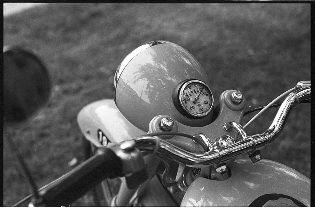 Gros plan sur le guidon d'une moto vintage, montrant un compteur et des détails chromés.