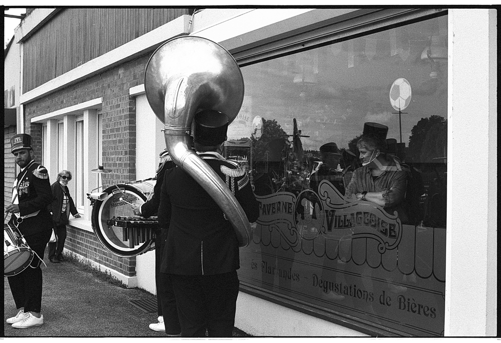 Un groupe de musiciens en tenue de parade devant un bâtiment, avec des personnes observant à travers une grande fenêtre.