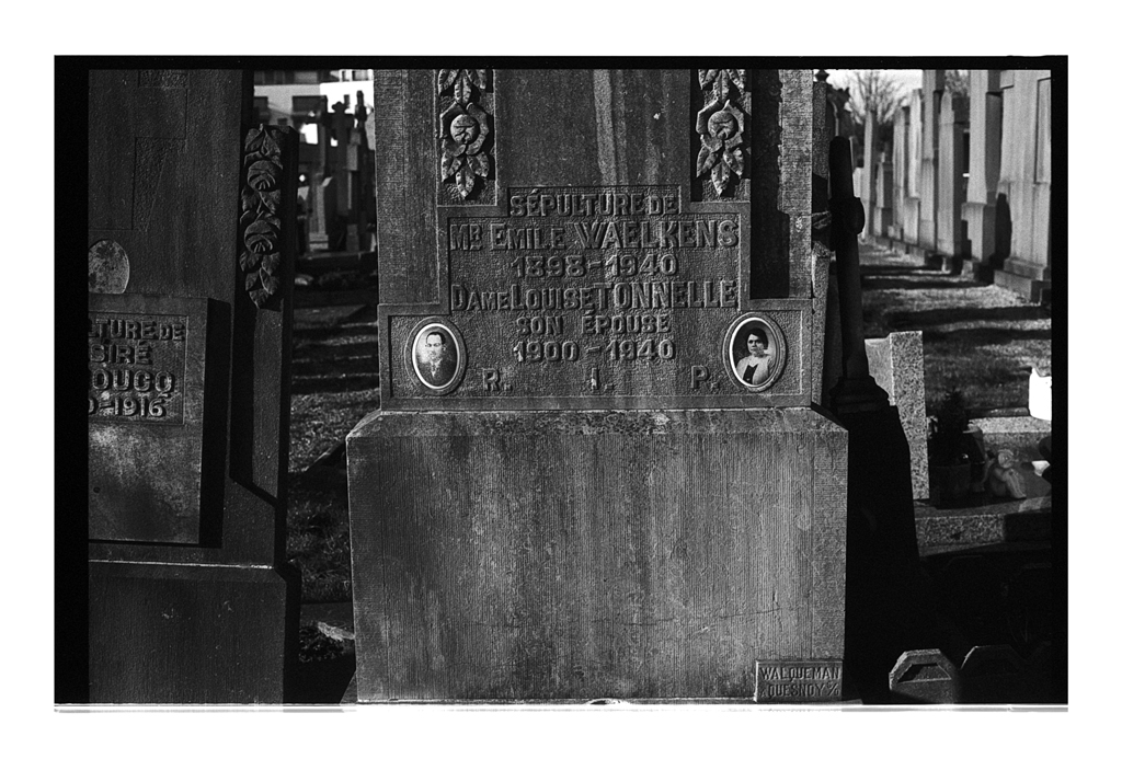 Pierre tombale ancienne avec inscriptions gravées et photos, dans un cimetière, capturée en noir et blanc.