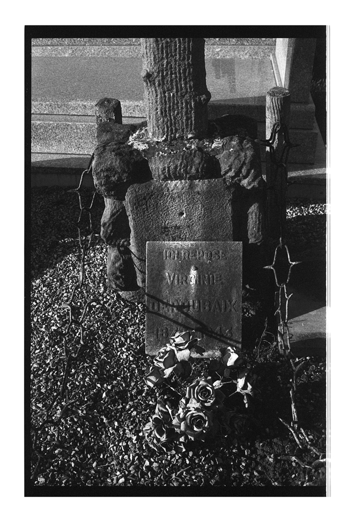 Pierre tombale ornée de roses sèches et entourée de fil de fer barbelé, dans un cimetière.