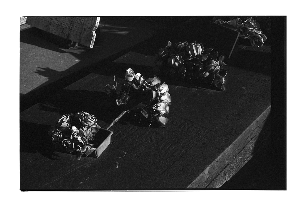 Photographie en noir et blanc d'anciennes pierres tombales avec des couronnes de fleurs, capturée dans un cimetière.