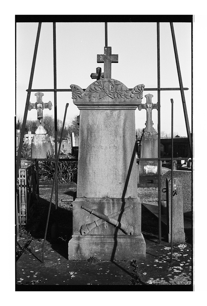 Une pierre tombale ancienne dans un cimetière, ornée de croix et de motifs floraux, avec un éclairage naturel mettant en valeur les détails et textures.