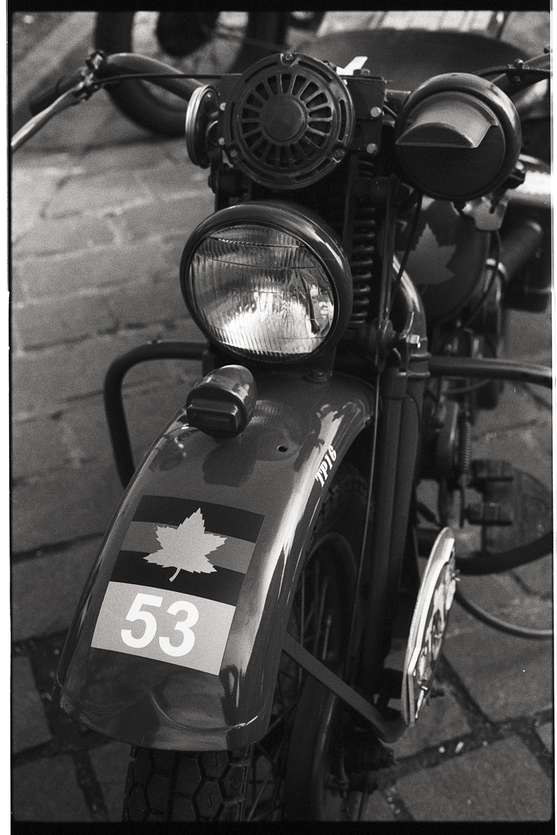 Gros plan sur une vieille moto avec un phare et un klaxon, ornée d'un autocollant de feuille et du numéro 53 sur la protection de la roue avant.