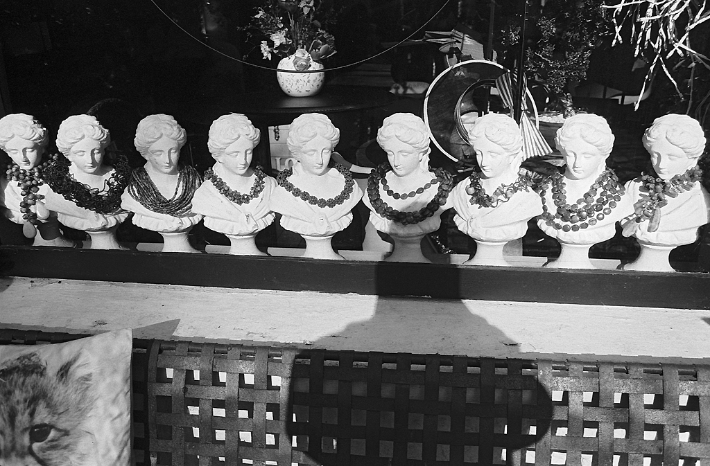 Une série de bustes en plâtre de femmes ornés de colliers, disposés sur une étagère, avec des ombres projetées en arrière-plan.