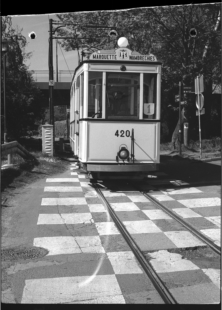 Un tramway circulant sur des rails sur une route avec un marquage au sol en damier, sous un ciel dégagé.