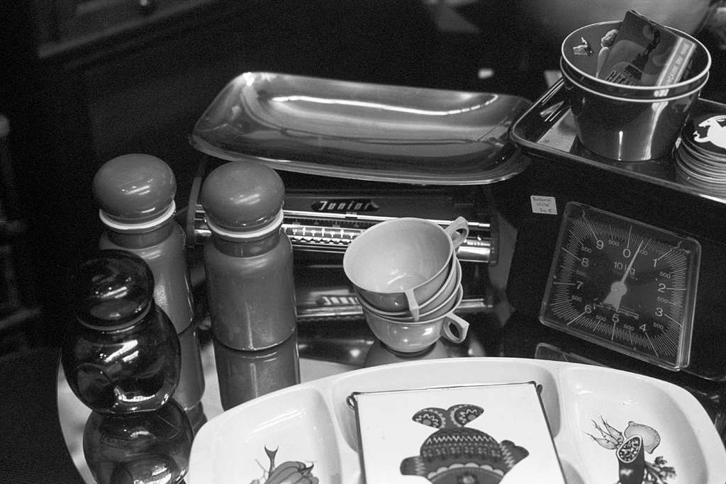 Une composition d'objets vintage comprenant des bouteilles, des tasses et une balance, photographiée en noir et blanc.