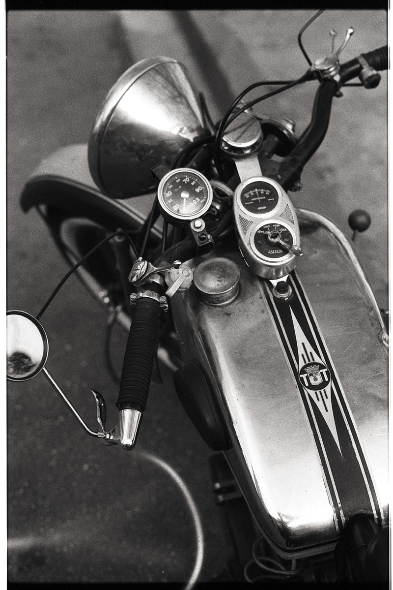 Détails d'une moto vintage avec un réservoir en métal, des instruments de mesure et un guidon, photographiés en noir et blanc pour un effet rétro.