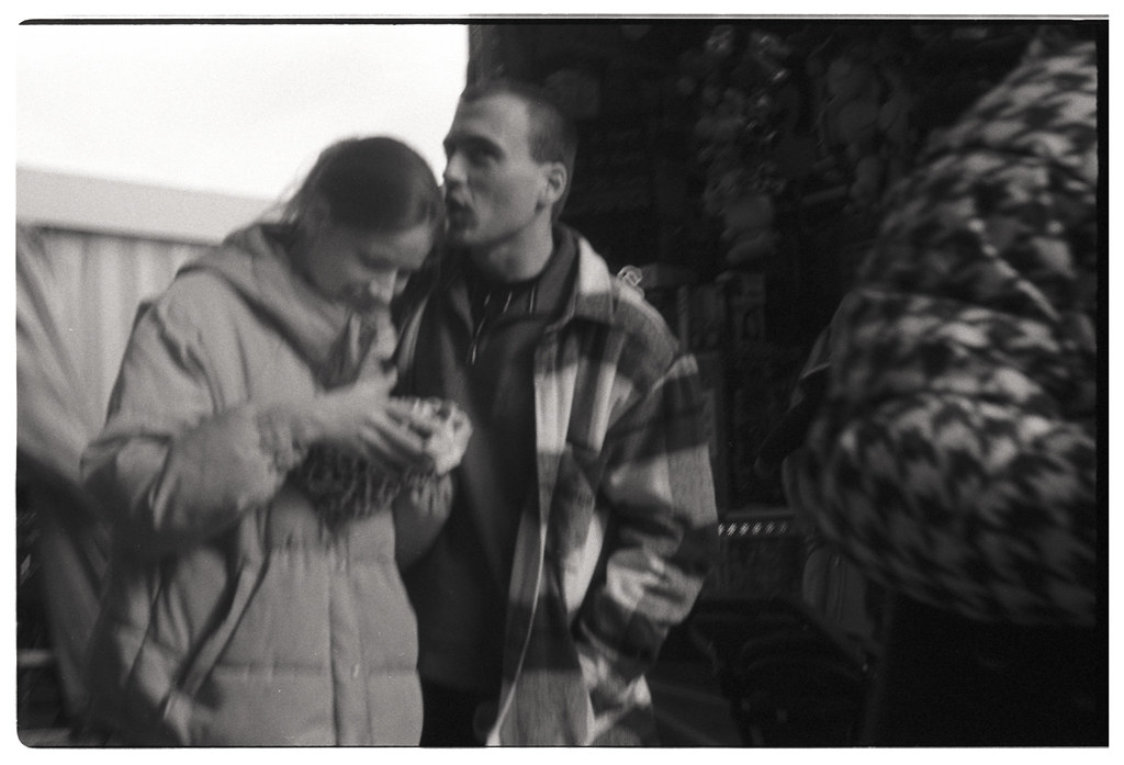 Photographie en noir et blanc d'un couple dans un marché, l'homme chuchote à l'oreille de la femme qui tient un bol.