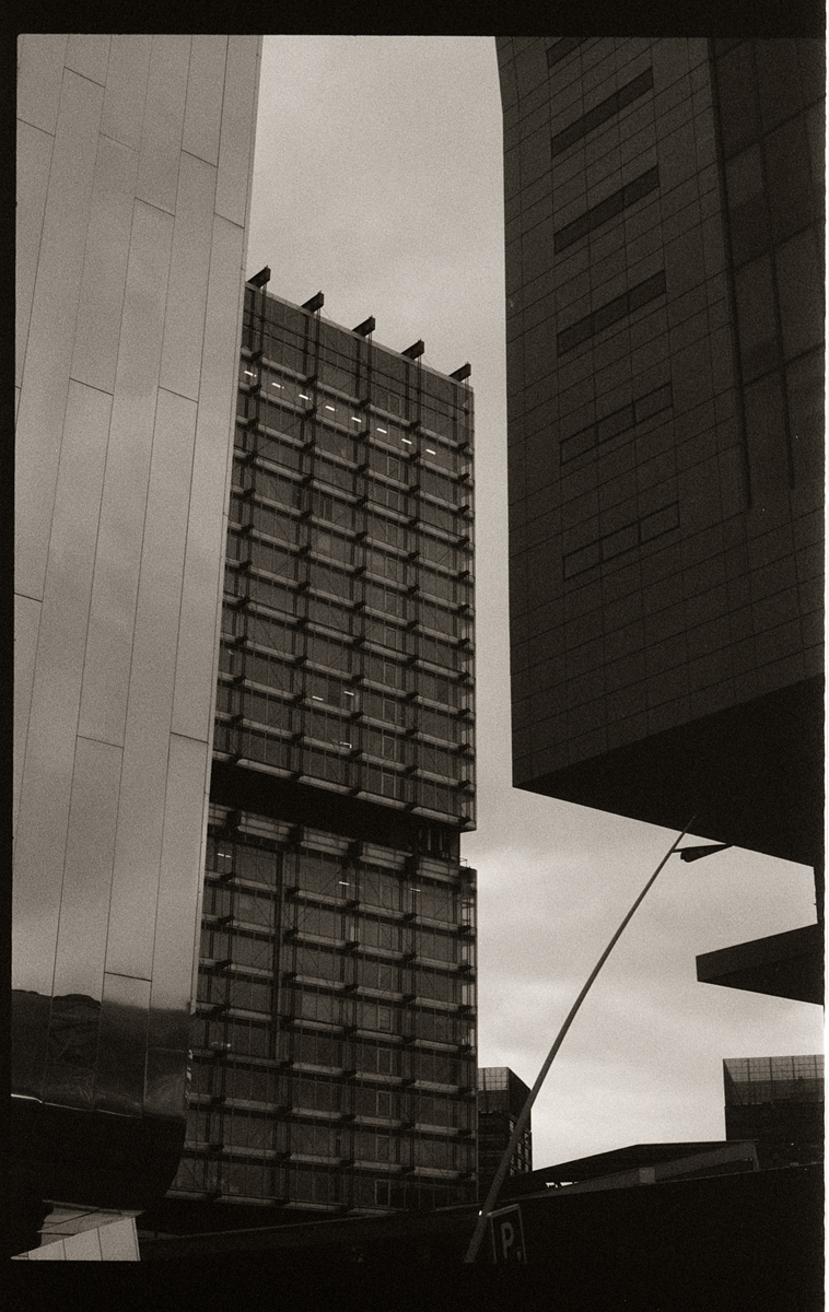 Photographie en noir et blanc d'immeubles modernes, capturant des lignes géométriques et des textures variées sous un ciel nuageux.