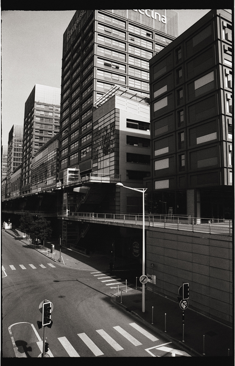 Vue urbaine en noir et blanc avec des bâtiments modernes, des panneaux de circulation et une route déserte.