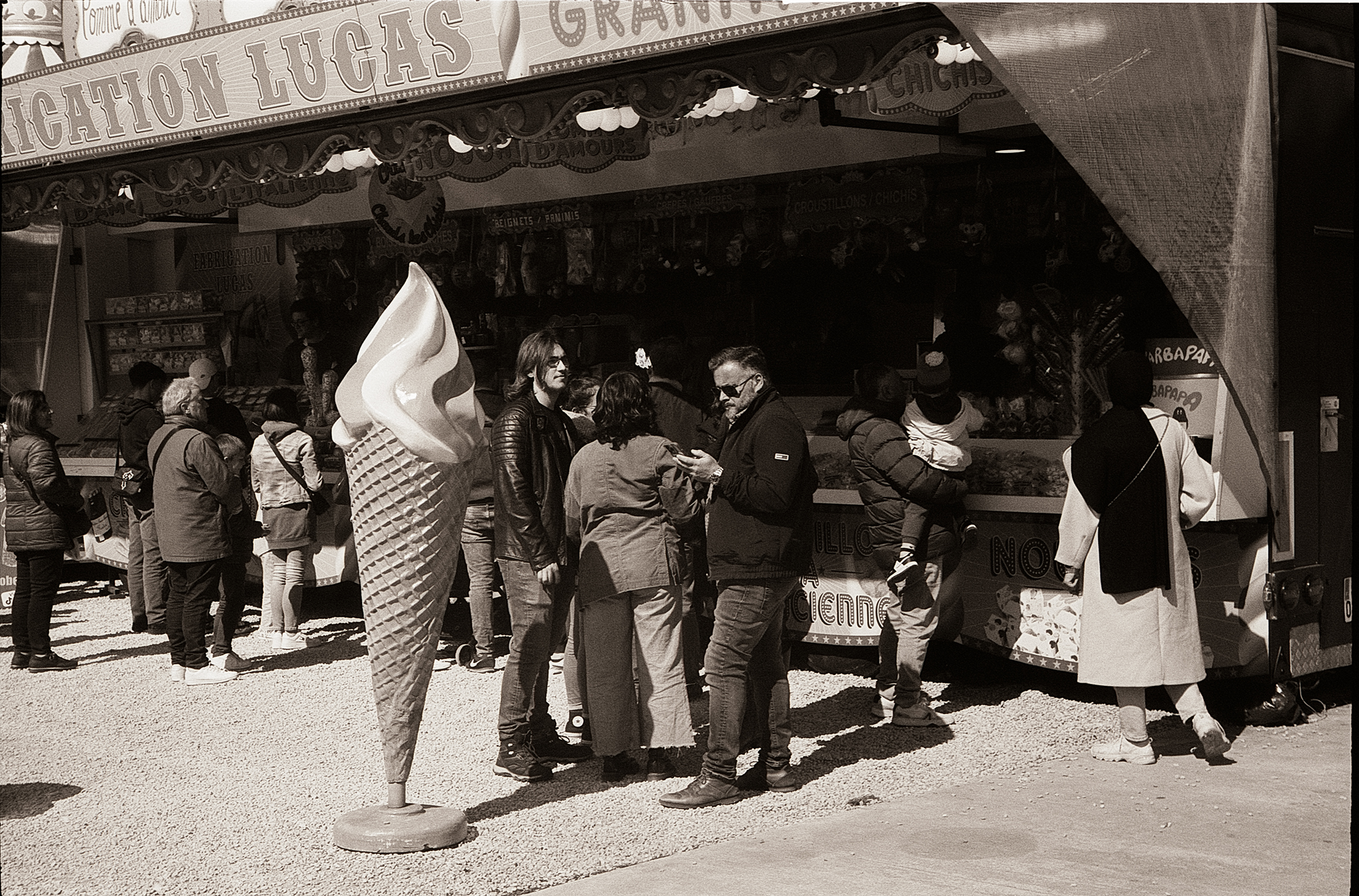 Scène d'une fête foraine à Lille avec des gens autour d'un stand de nourriture, un grand cornet de glace en arrière-plan.