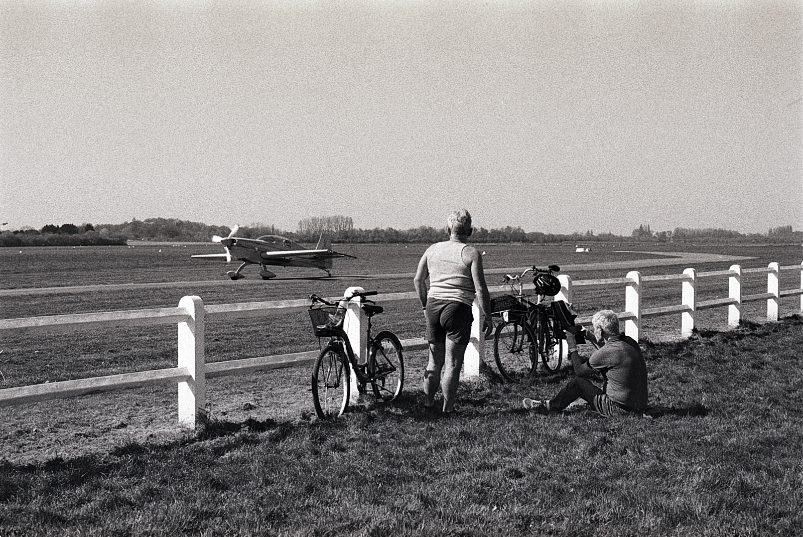 Photographie argentique noir et blanc de l’aérodrome de Bondues, avec avion d’école et vélos modernes ; grain marqué et contraste dense évoquant une esthétique rétro.