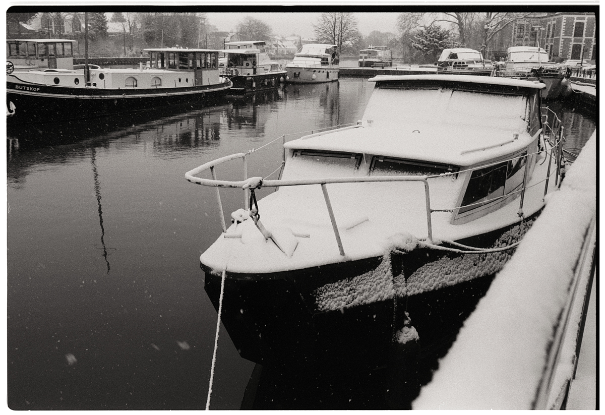 Photographie argentique style rétro de bateaux et péniches sous la neige dans un petit port de plaisance.